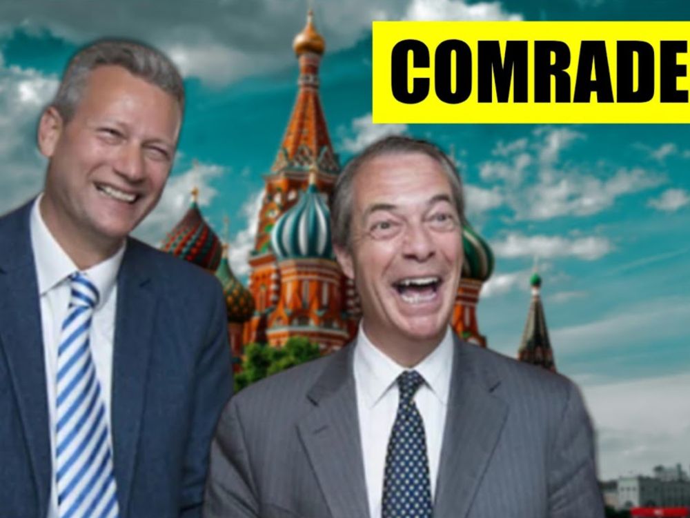 Two men in business attire are standing in front of a digitally added backdrop of Saint Basil’s Cathedral in Moscow. Both are smiling broadly, with the man on the right laughing with his mouth wide open. The sky behind them is bright with scattered clouds. In the upper right corner, there is a bold yellow rectangle with the word “COMRADE” written in large black letters. The overall composition gives the impression of a satirical or edited political image.