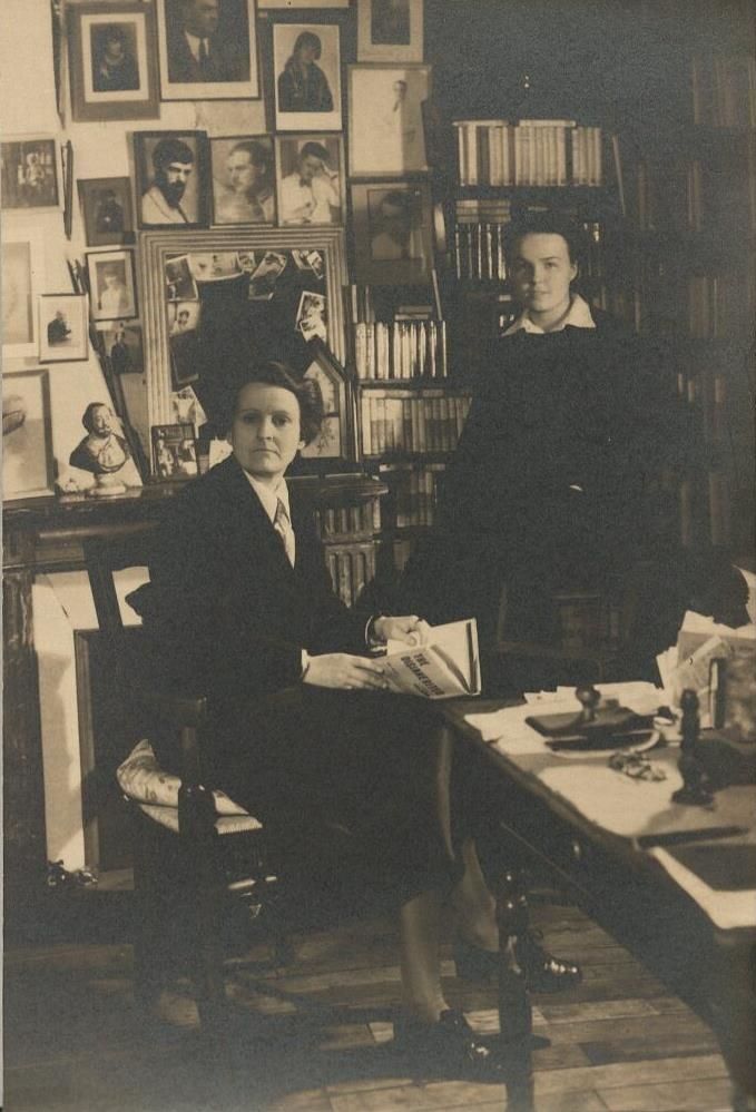 Postcard portrait of Sylvia Beach and Jane van Meter in Shakespeare and Company bookshop, with portraits of writers, including H. D., William Carlos Williams, and Bryher, D. H. Lawrence, Ernest Hemingway, and James Joyce (among others), visible on the wall behind them. Joyce is the figure in white with his hand held to his head. Circa 1934. Jane van Meter Collection. MS 383, Box 1, Folder 22.