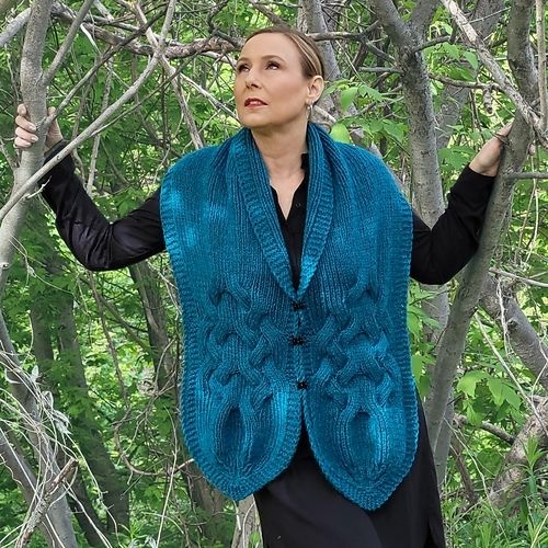 Myself, standing in a thicket of small trees, wearing a black dress with a deep teal coloured wrap over my shoulders and fastened at the front.