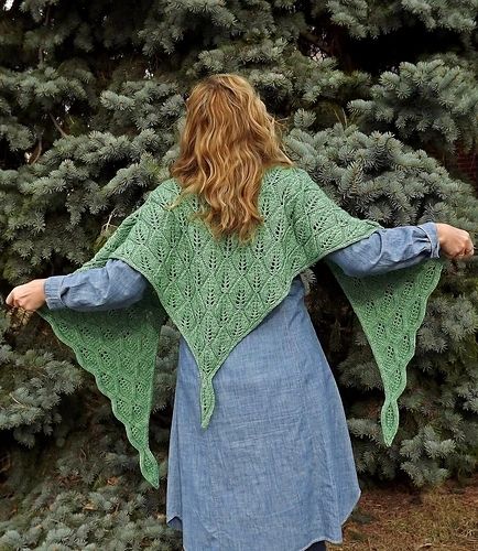 I stand back-to wearing a bright green knitted shawl with an all over leaf pattern, against the background of a large spruce tree.