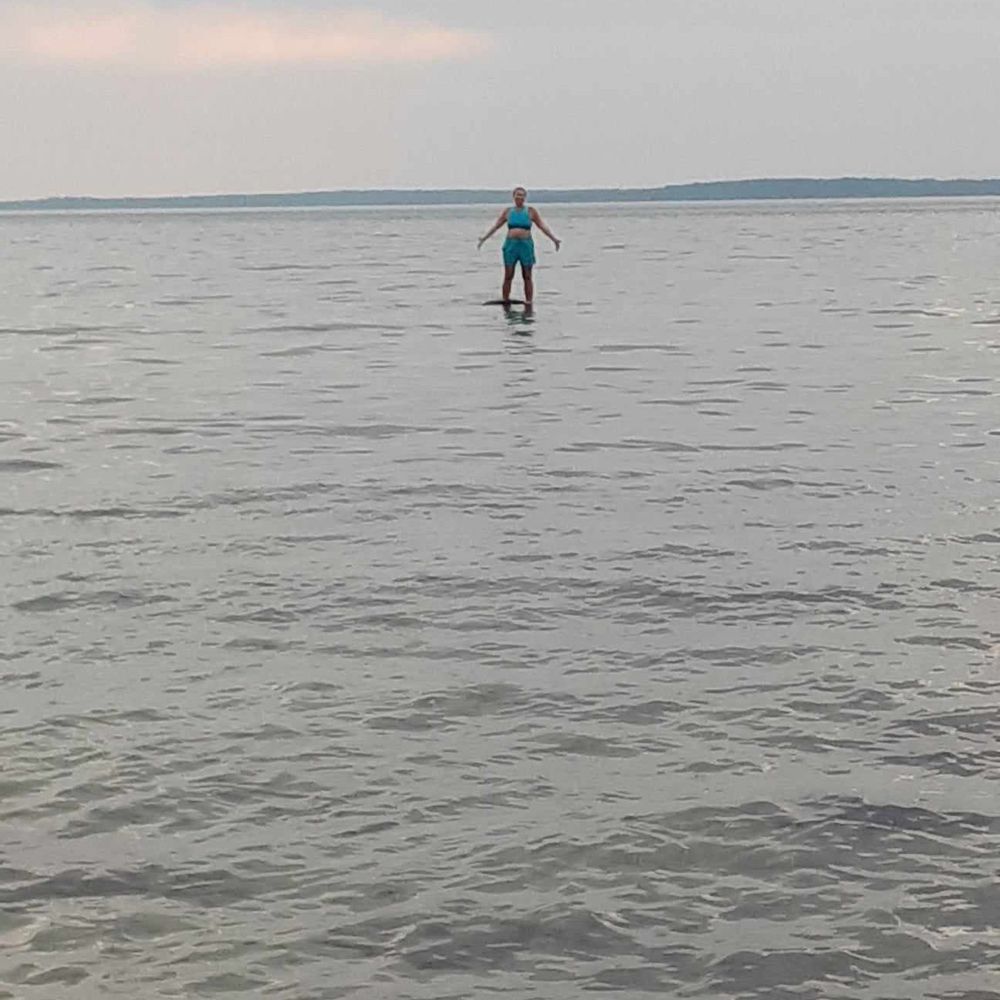 Myself, far in the distance, standing in the middle of the water (on a hidden rock) on a hazy summer day.