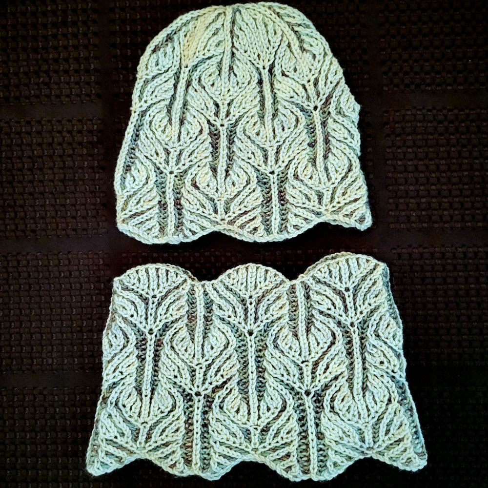 A flat lay photo of a 2 colour brioche knit hat and matching cowl, in colours of cloud formation and winter blue, on a black background.