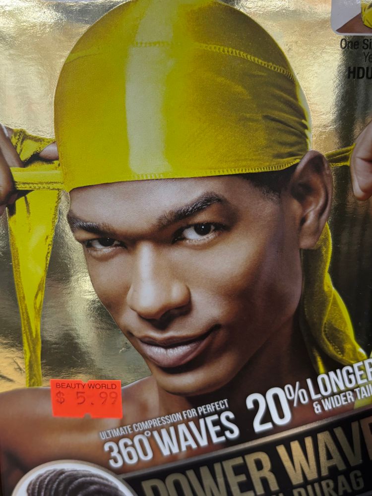 Light skinned Black man smizing (smiling and smirking) at the camera while tying a neon yellow durag. He has very high cheekbones. 