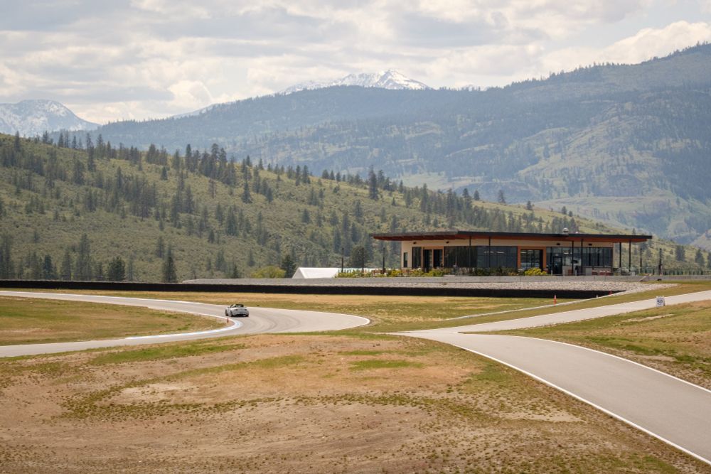 A grey Mazda MX5 on a race track. The Area 27 Clubhouse and tree lined mountains in the distance. 