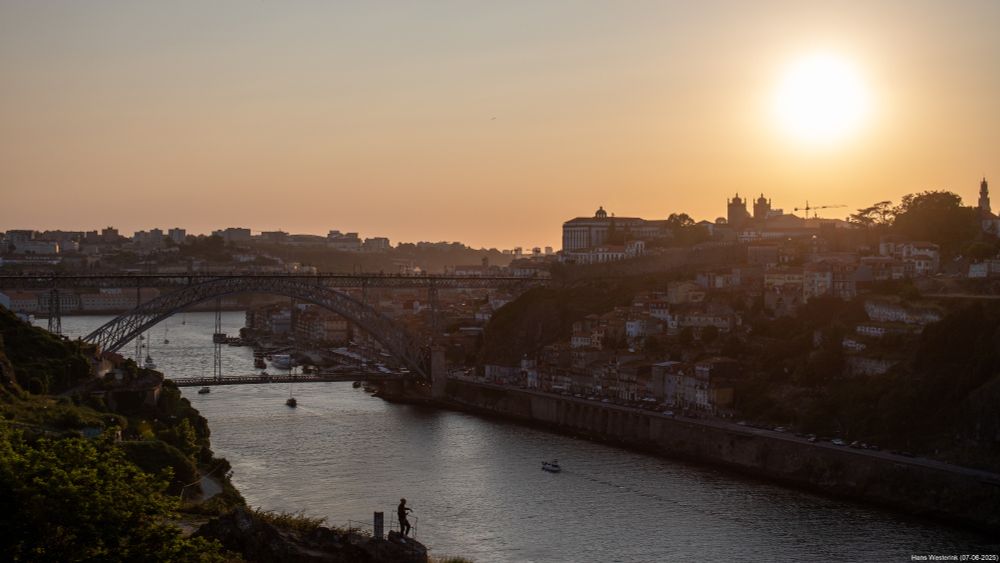 River with bridge. On the other side buildings and a setting sun, still above the city