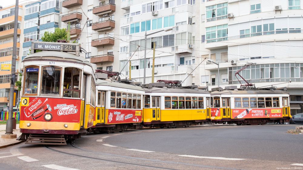 Four two axle yellow and white trams in a curb. Appartment buildings in the background 