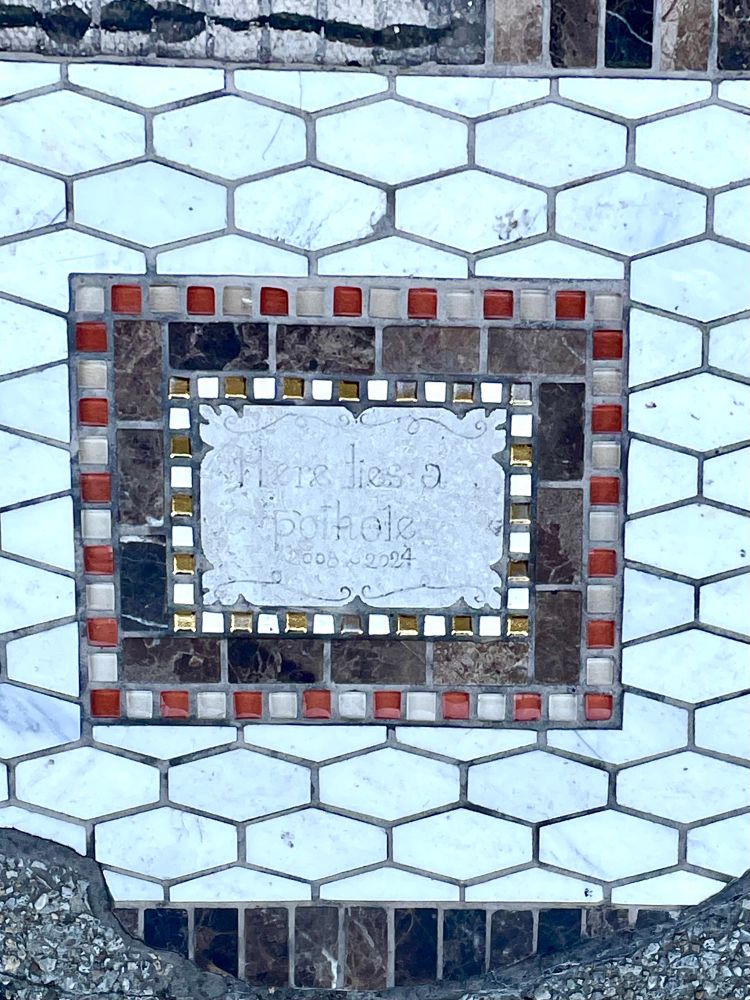 The epitaph in the middle of the mosiac: Here lies a pothole 2005-2024