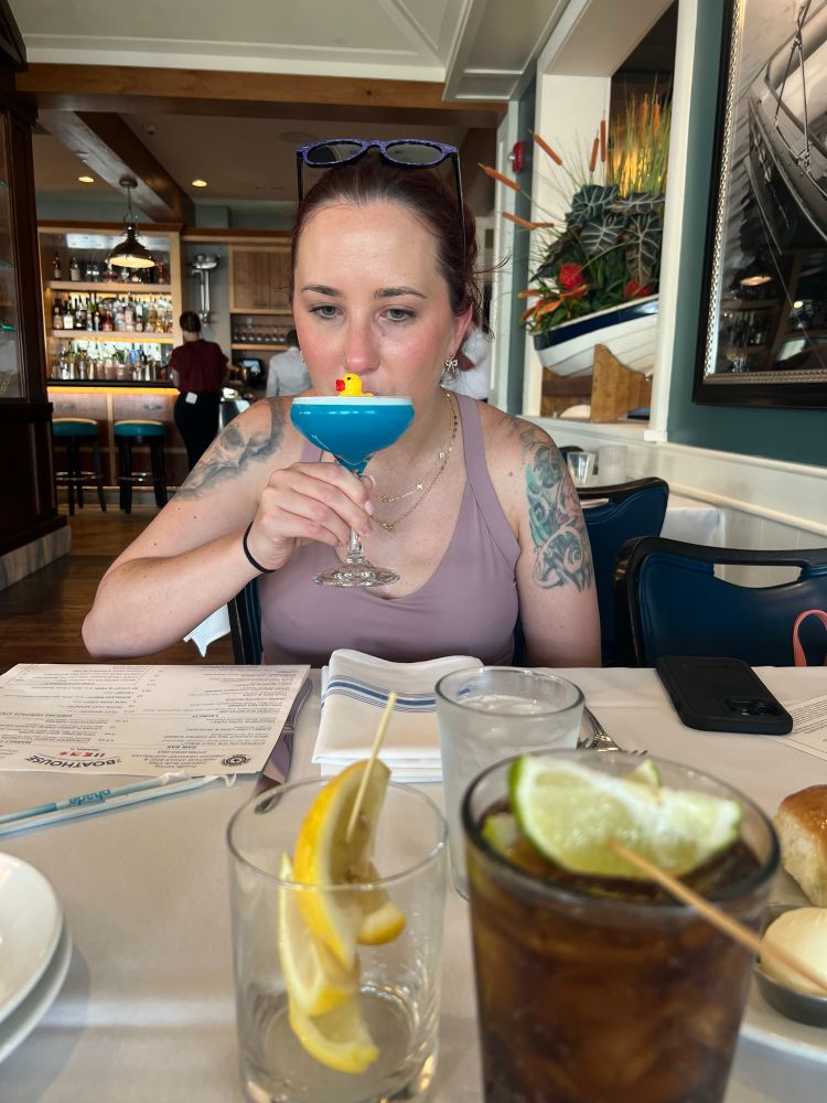 Woman in purple dress drinking blue martini drink with rubber duck in it 