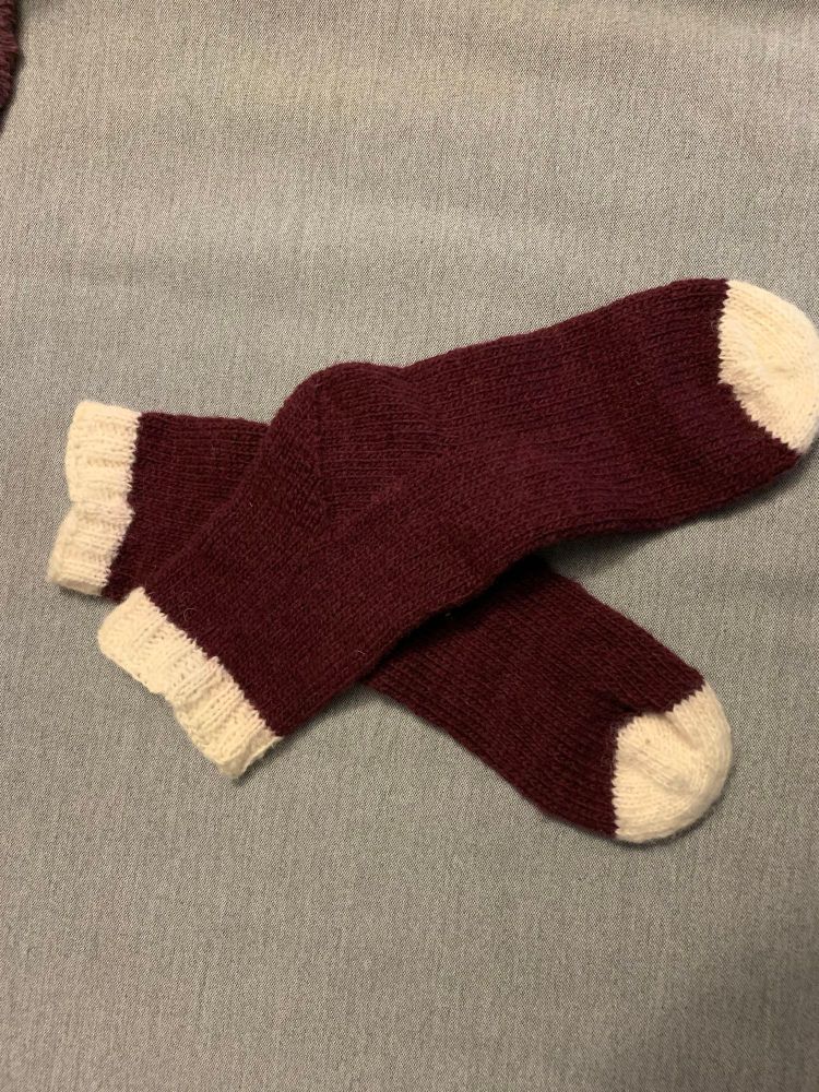 A pair of burgundy socks with white toes and cuffs on a grey background. 