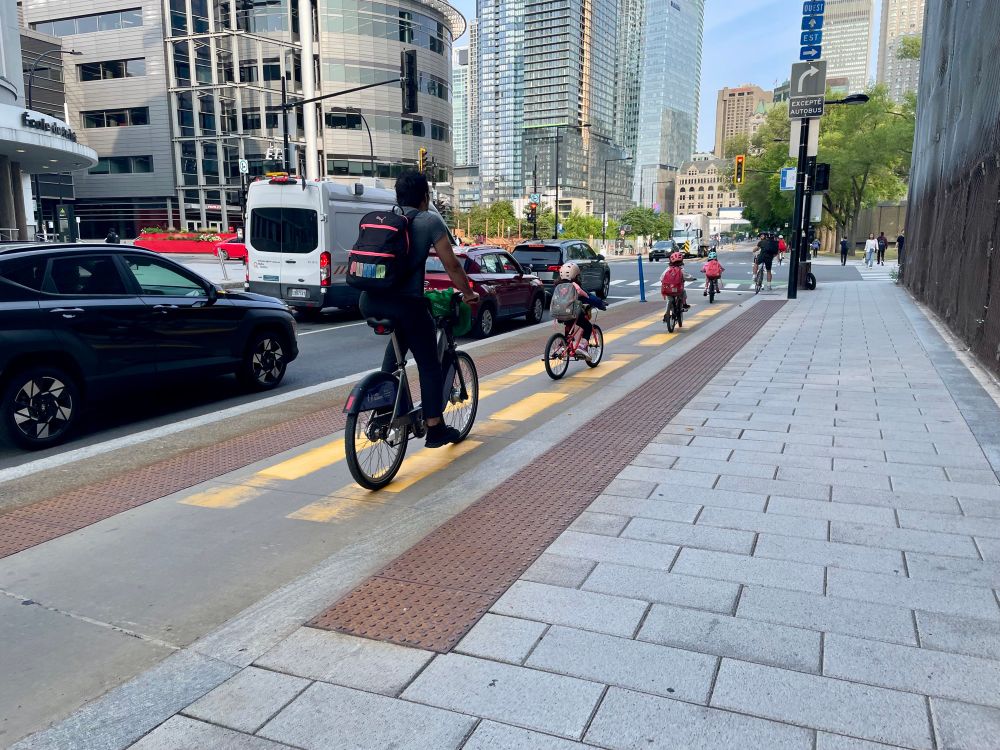 Une file de personnes à vélo dont des enfants sur piste cyclable de la rue Peel dans le quartier Griffintown à Montréal