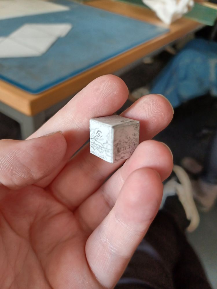 A small paper cube with Flesh Panopticon's face from ULTRAKILL drawn on