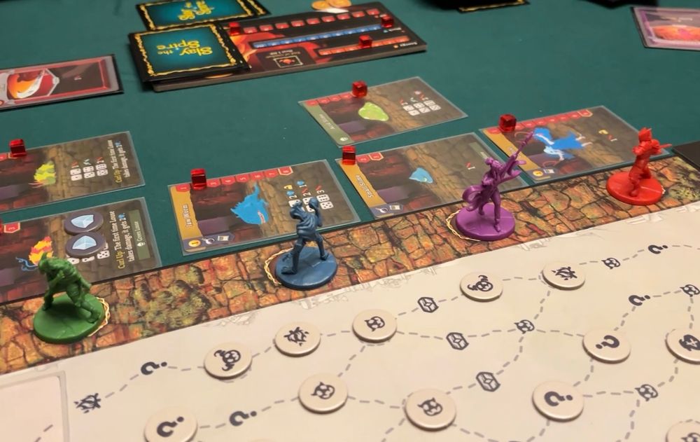 Slay the Spire board game set up on a table. A board, four minis on it, and cards of enemies placed next to the minis.