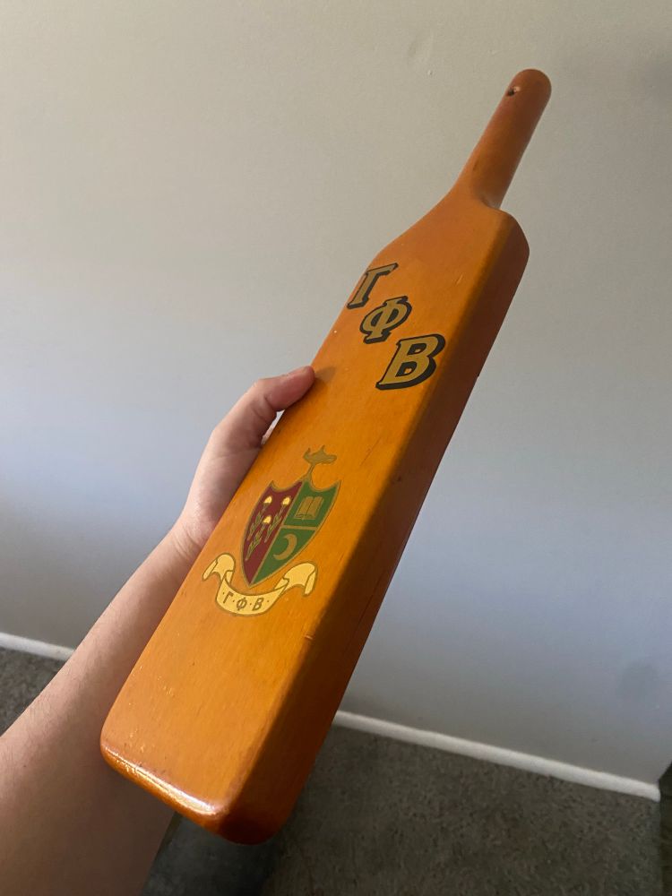 SHE THICC! A reddish/brown sorority paddle with "Gamma Phi Beta" in greek letters printed on it.