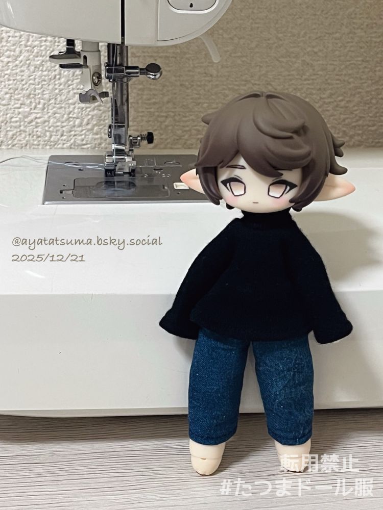 ミシンの前に立たせたブラインドドール　秘境巡礼・アスタ
茶色いショートカットのドール。黒いハイネックのトップスと、デニム風のズボンを着用