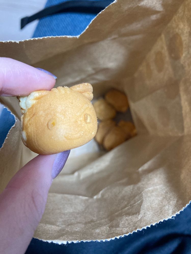 Hand holding Phoenix Wright from Ace Attorney as baby castella in front of bag containing other castella characters.