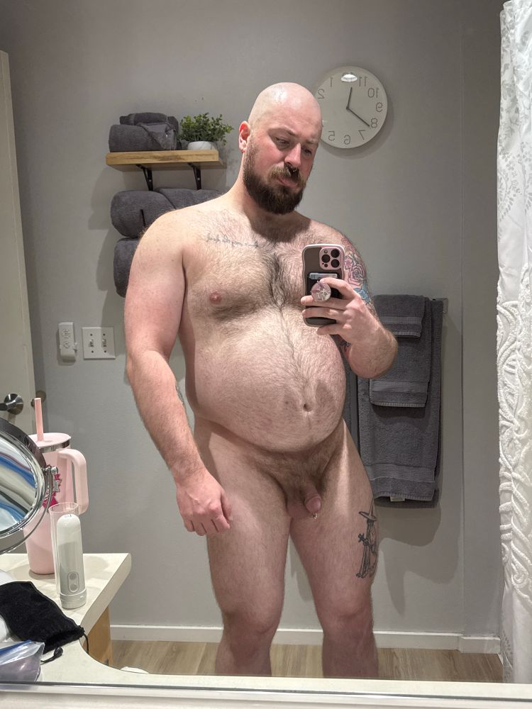 a fat muscle dog stands in a bathroom taking a photo of their naked body from the knee up. they are sweaty and their tongue is out 