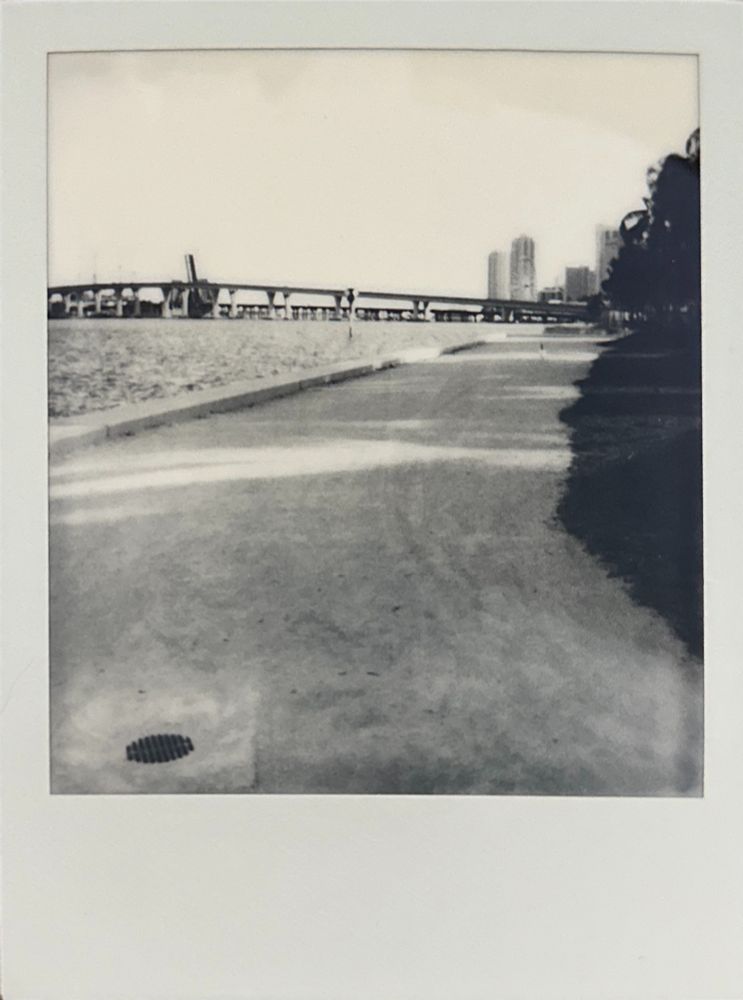 Polaroid black and white image of a bay front park walkway with a causeway in the background.
