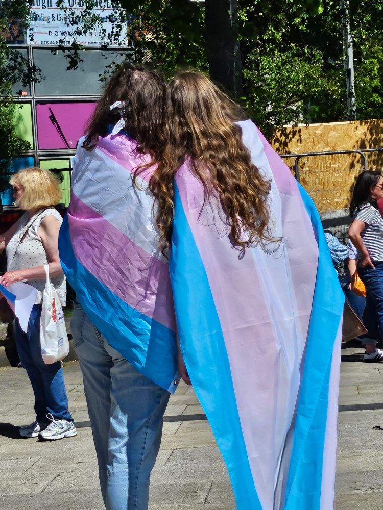 Two people draped in trans flags 