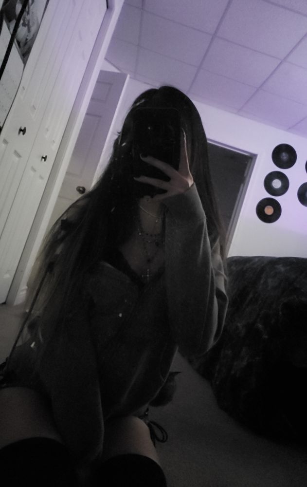 Mirror selfie of girl sitting on floor in emo fashion, with phone covering face.