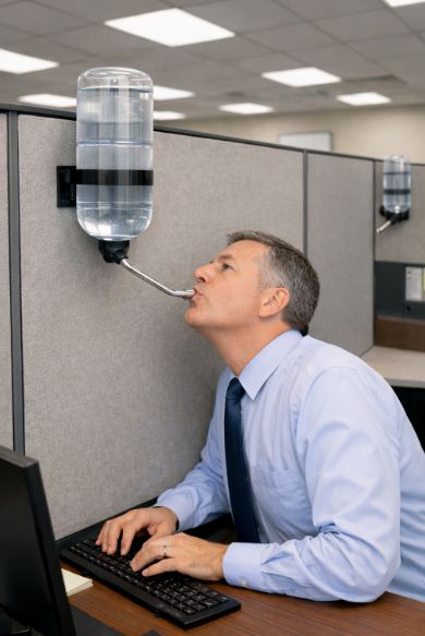 A professional man in his cubicle, drinking from a track-ball water dispenser as would a caged hamster.