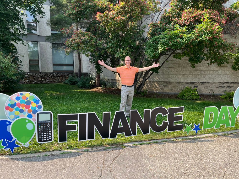 Me standing behind a large lawn sign that says “Finance Day”