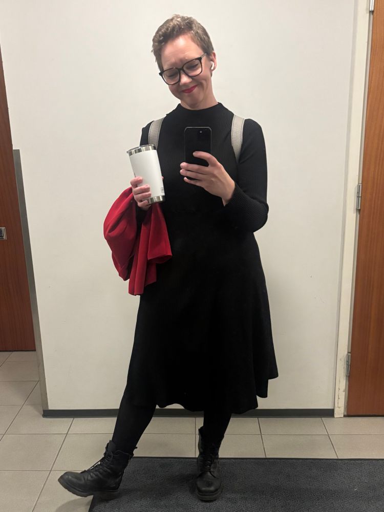 Mustaan pukeutunut nainen kahvikuppi kädessä. 