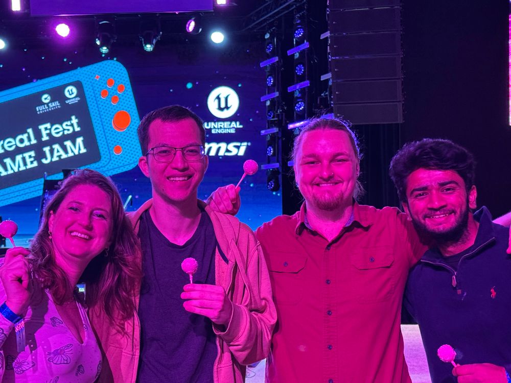 A group of four people—three men and one woman—stand smiling under purple lighting in front of the Unreal Fest Game Jam stage backdrop. Each person is holding a pink cake pop, celebrating their teamwork. The background features branding for Full Sail University, Unreal Engine, MSI, and the event’s retro game-themed graphics.