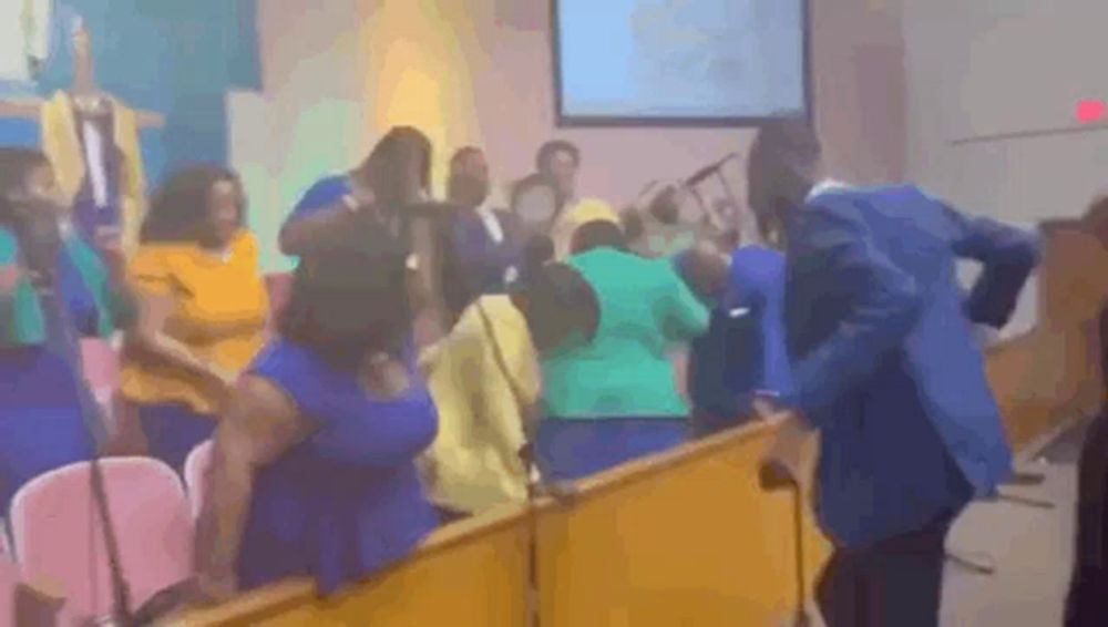 a group of people are dancing in a church while a man in a blue jacket stands behind them .