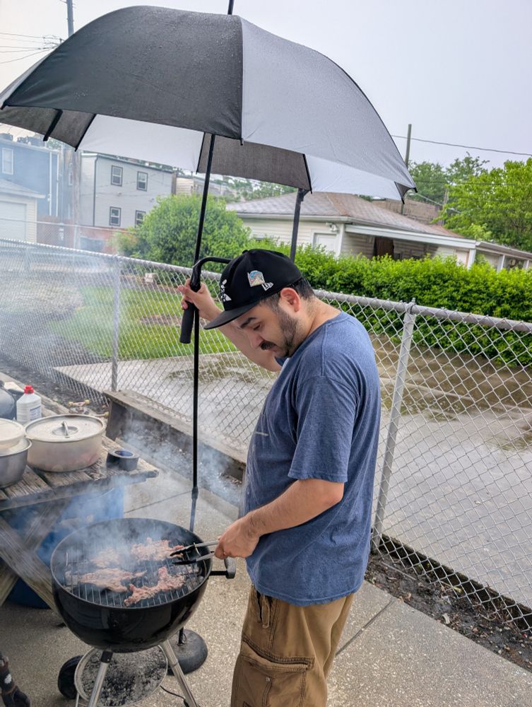 OP grilling skirt steak with a makeshift umbrella stand during a storm.