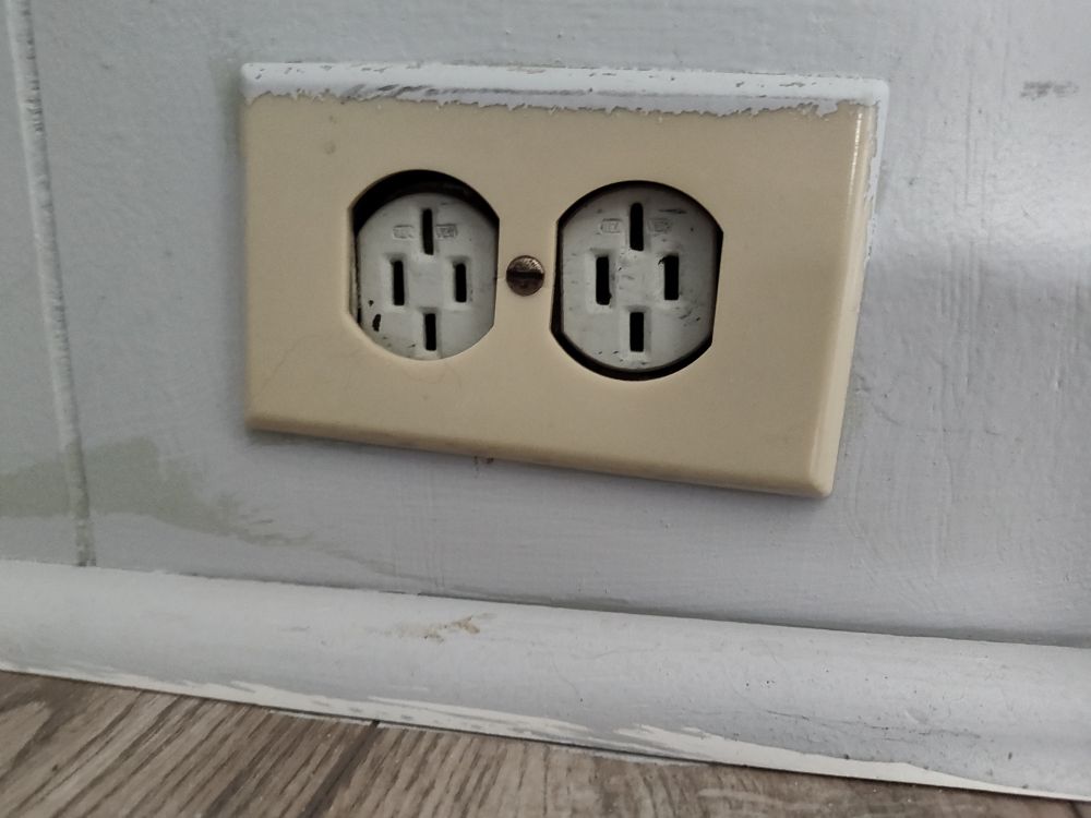 An electrical outlet in our apartment. It has the standard two vertical slots for a US plug, but also has two extra vertical slots where the ground prong would be.