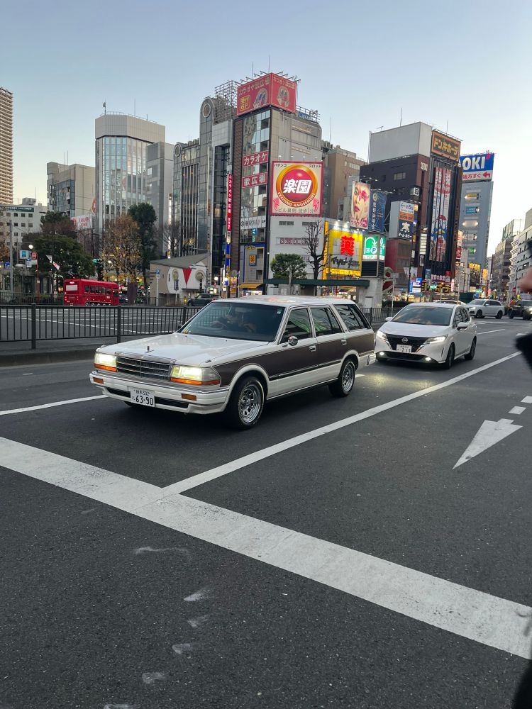 A white-and-wood-panelled mid-eighties Nissan Gloria wagon sitting pretty at a traffic light in Ikebukuro, Tokyo, Japan. 