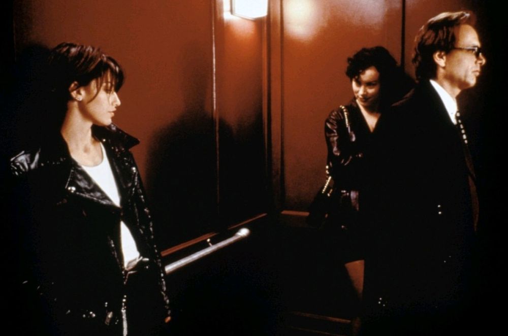 Still from the movie "Bound", butch Corky makes eyes at fem Violet behind the back of Violet's gangster boyfriend as the three stand in an elevator.