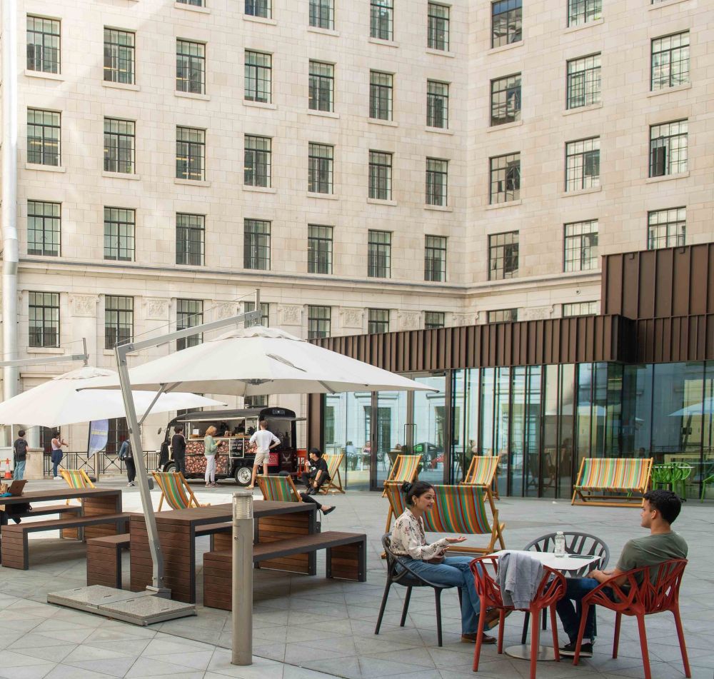 Bush house court yard on a sunny day, with students sitting at a table chatting.