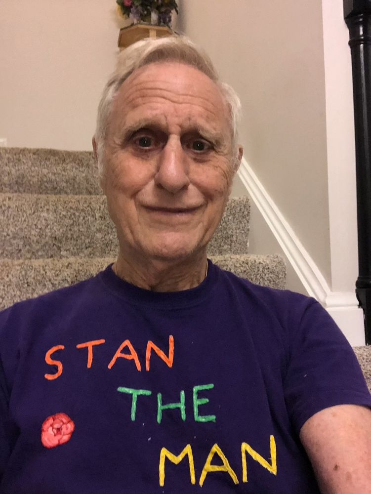Stanley smiling warmly, wearing a shirt with the words 'Stan the man' embroidered on it. Stan appears to be sitting on a staircase.