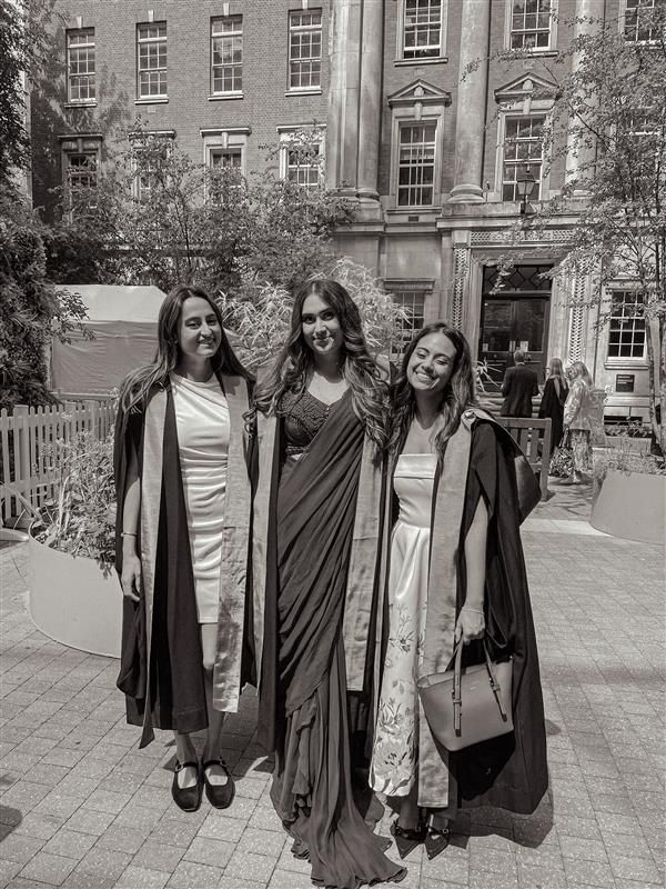 A black and white picture of three students dressed in graduation attire, smiling warmly, posing for a picture.