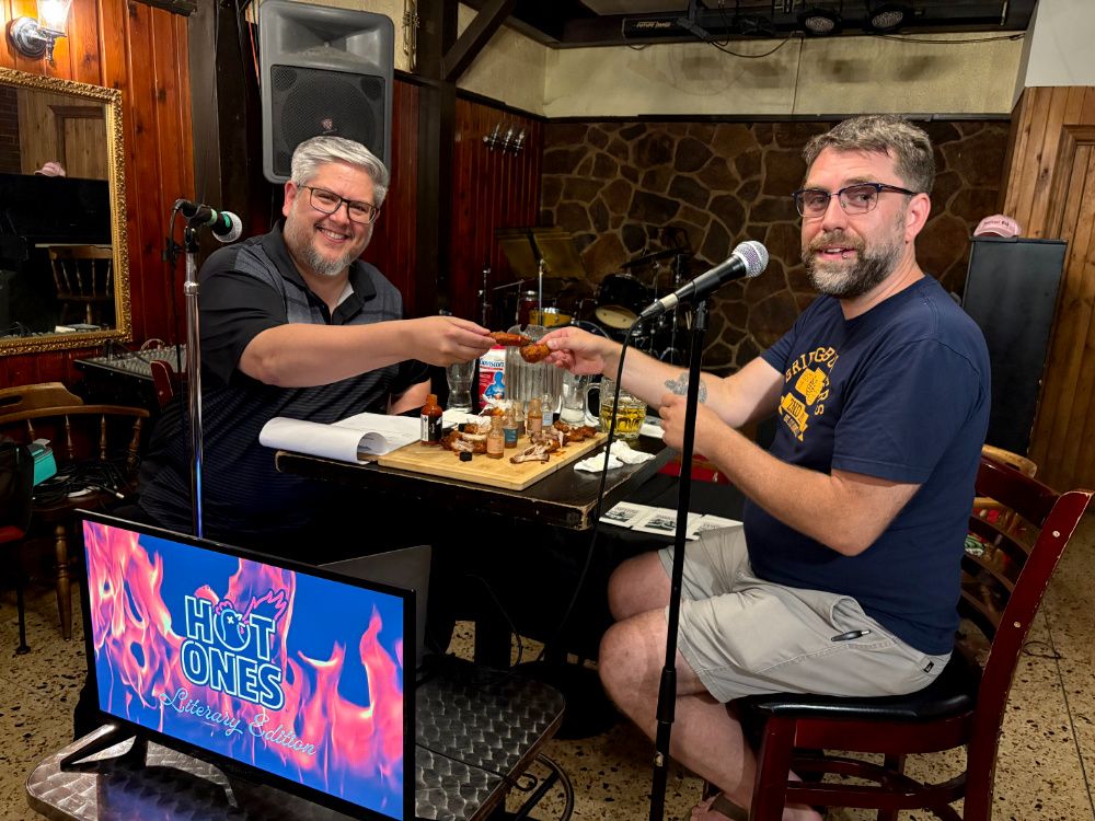 Two men (me and my friend Peter) sitting in a pub at a table with hot wings. There are microphones, and they are cheersing their hot wings.