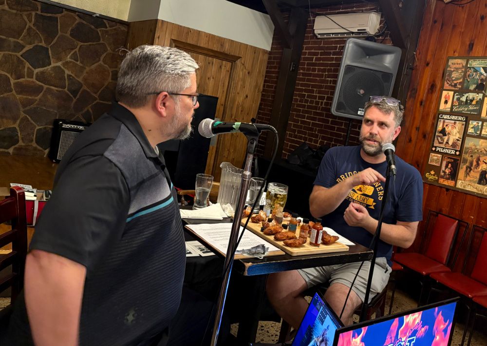 Two men (me and my friend Peter) sitting in a pub at a table with hot wings. They are talking into microphones.