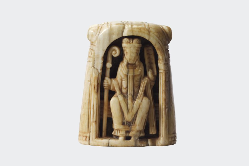 Pièce d’échecs en ivoire représentant un évêque dans une niche. Il porte un vêtement liturgique, une mitre et tient une crosse et un livre ouvert.