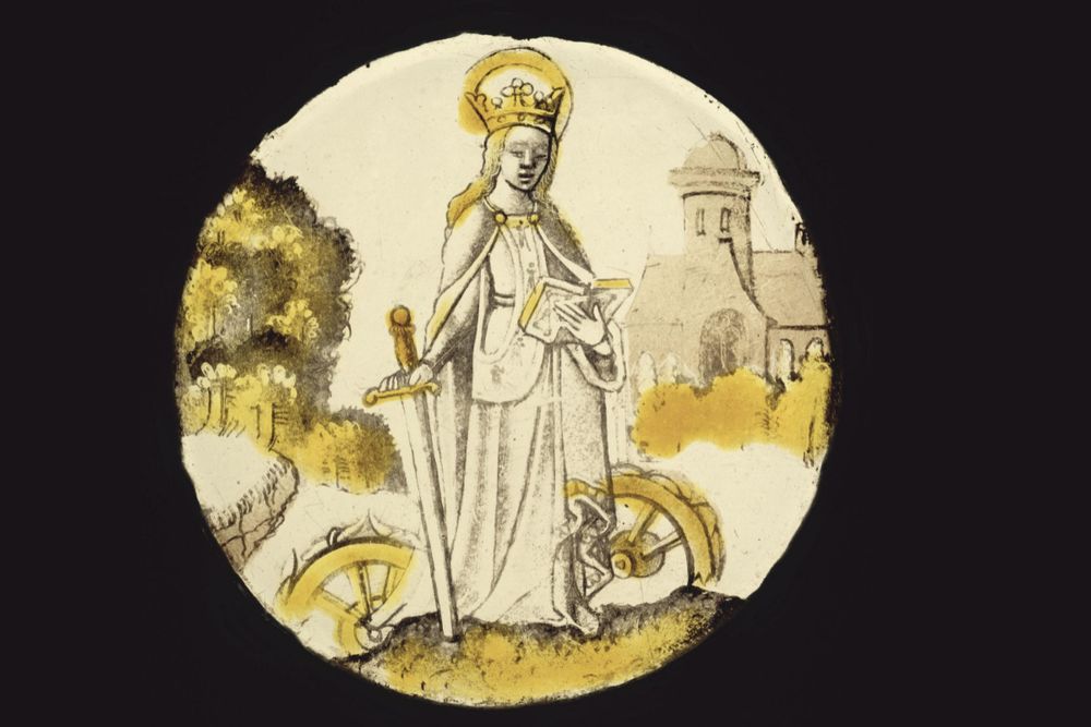 Vitrail jaune et gris représentant une femme tenant une épée dans une main et un livre dans l’autre, deux roues sont à ses pieds