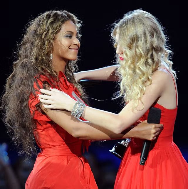 Beyonce and Taylor Swift, both wearing red, hugging on stage at the 2009 VMAs