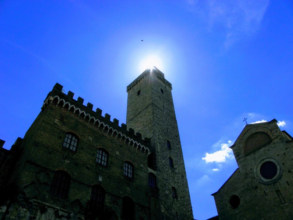 Die Sonne schaut über die Ecke eines Turmes.
