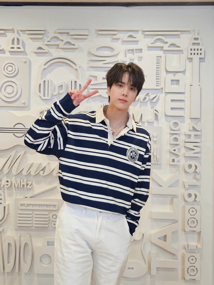 Younghoon in a blue striped shirt doing a peace sign, from farther away
