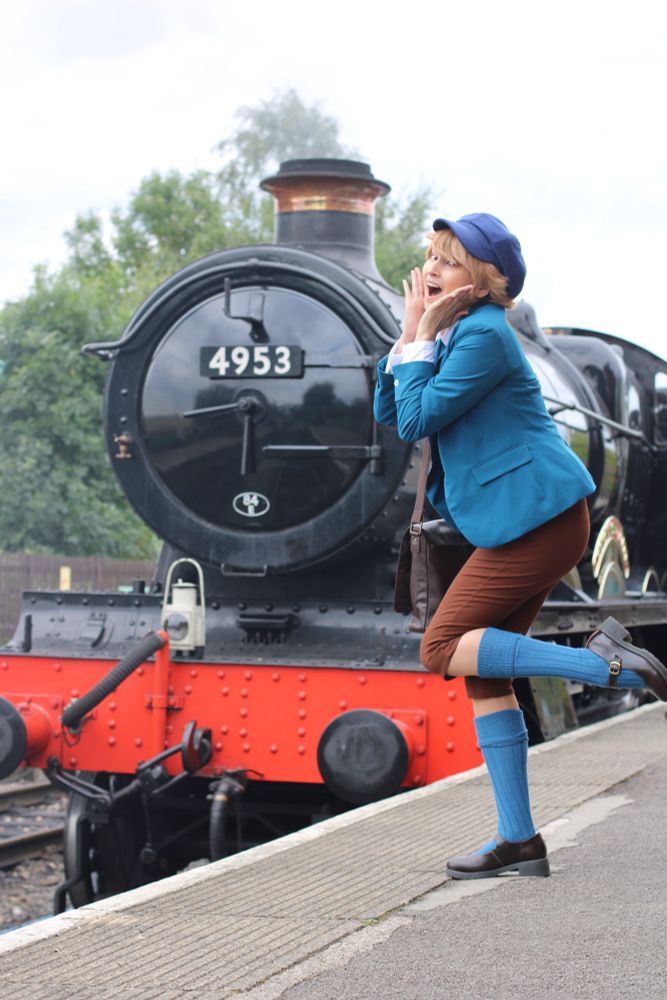 andy as clive posing with a steam train (they are looking very excited with their hands by their chin and one leg kicked up) 