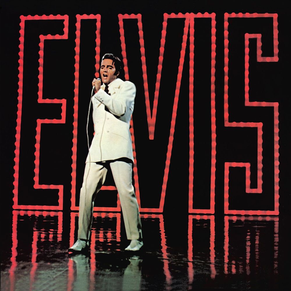 Elvis Presley, in a white suit, singing, in front of giant red lights that spell out his name. Elvis is everywhere. 