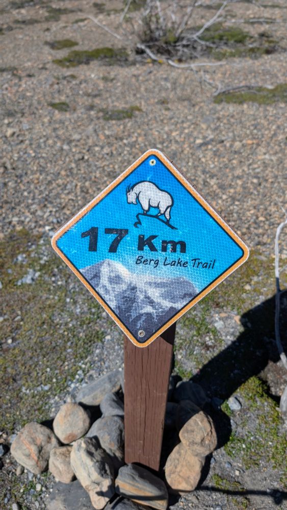 Trail sign of picture of mountain goat and 17 Km on blue sky. Mountains frame the bottom.
