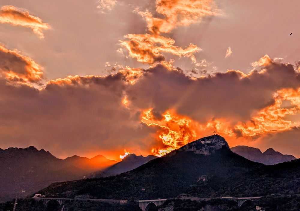Mountains with orange sun setting behind darker orange clouds. 