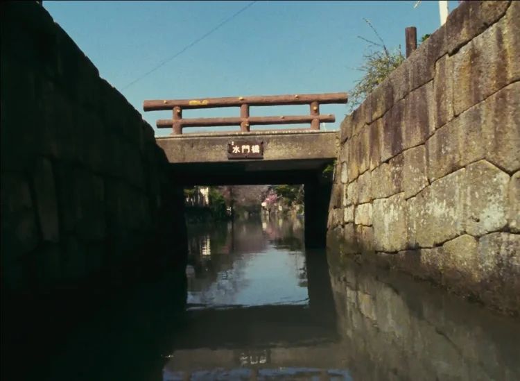 Image from The Story of Yanagawa's Canals, showing a point of view from a boat in a canal with high walls to the left and right and a bridge overhead