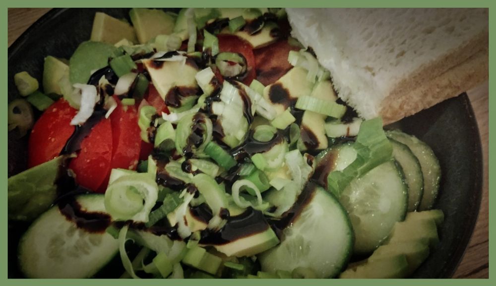 Salatteller mit Tomate Avocado Gurke und Zwiebeln mit Knoblauch Zitrone Dressing und etwas Basamico crema rechts oben zwei Scheiben Toast