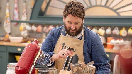 Jim Howick in the Bake Off tent wearing a Stand Up To Cancer apron.