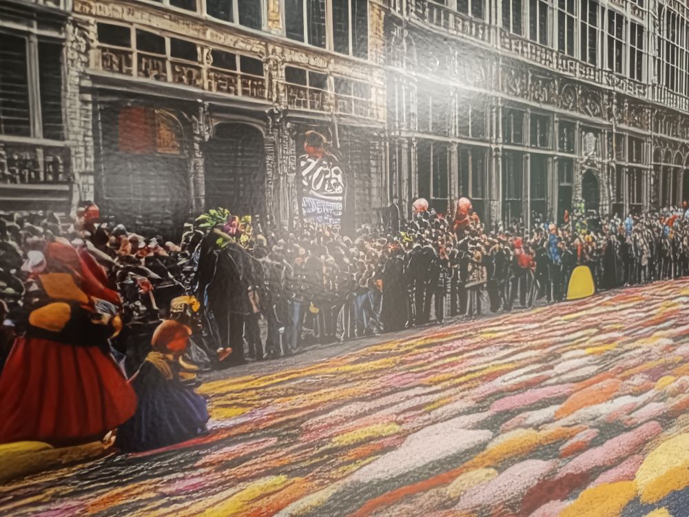 Closeup of the "people" on the "picture" which is a nightmarish blotchy mess, and there are mighty weird "people" in there, and for some reason the flowers are in a different perspective than the people and buildings...

the people are so messed up, they would probably claim it's a "painted" style, but the flowers just in front of the people look like it's trying to imitate a photograph, but then from a 1998 era digital photocamera or webcam... on top of that, the perspective is "offensively" wrong (don't know how else to describe this feeling from my brain and heart that just want to reject the existence of this PoS...

then there are the buildings... oh my god the buildings... 

you see, at first view they look "a bit artst" but then you start looking at the lines and you'll see that they are all a single mass of a seemingly living building... 

it's a horrible blend of Gaudi and H.R. Giger, together building a Grand Place that's worthy of a Cthulhu novel where the buildings surrounding a Grand Place covered in colourful flowers eat humans and feast on their souls!